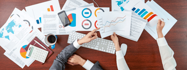 A desk covered in reports, a calculator, a keyboard, a phone, and a cup of coffee.