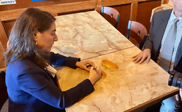 A woman signs a hot dog bun at a table in a restaurant.