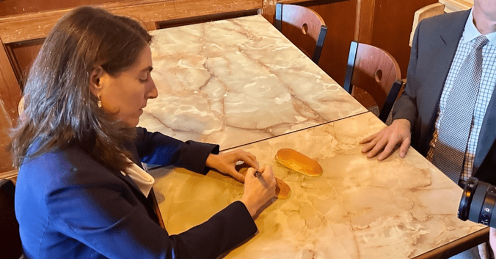 A woman signs a hot dog bun at a table in a restaurant.