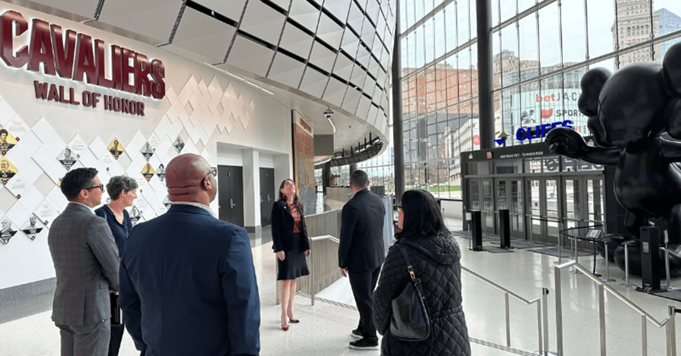 A group of people stand in an arena with large glass windows.