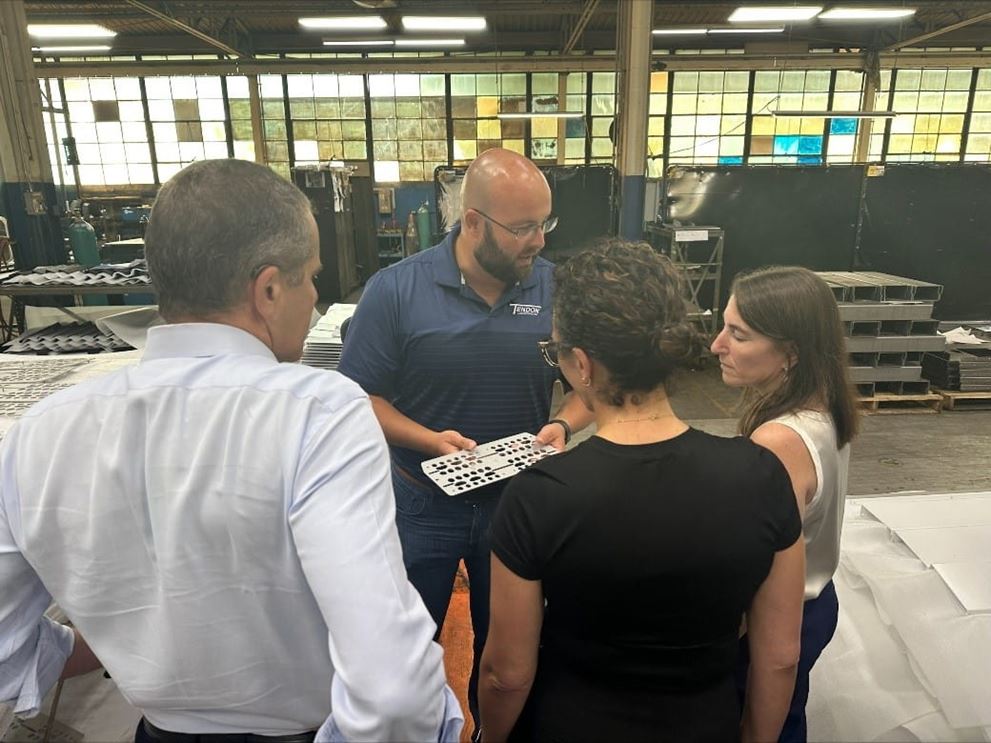 A group of people look at a metal piece in a factory setting