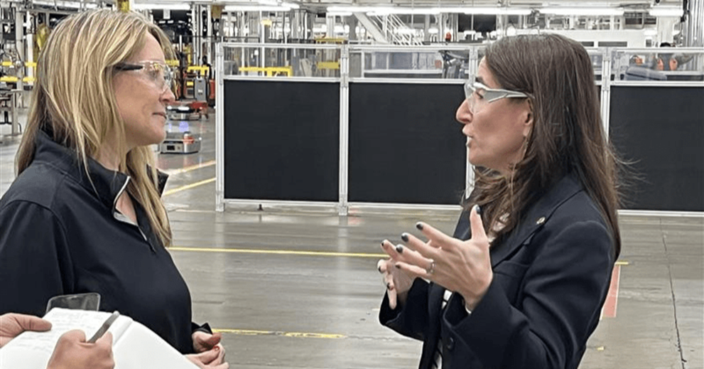 Two women talk on the floor of a vehicle assembly plant.
