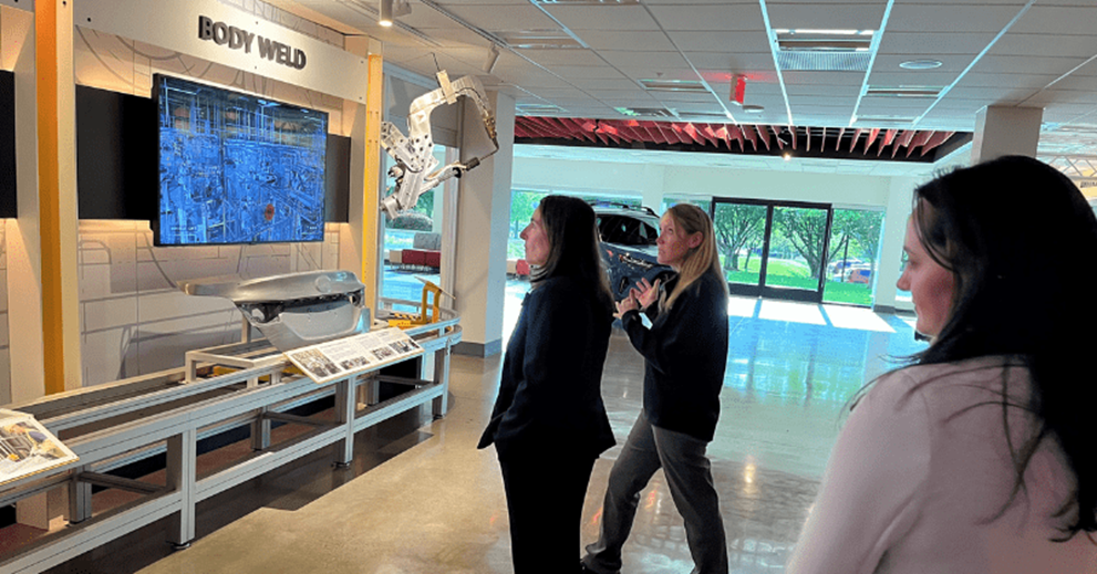 Several women view an exhibit on auto assembly.