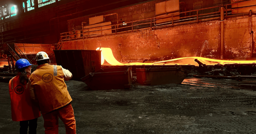 Two people in a factory setting watch a piece of molten steel
