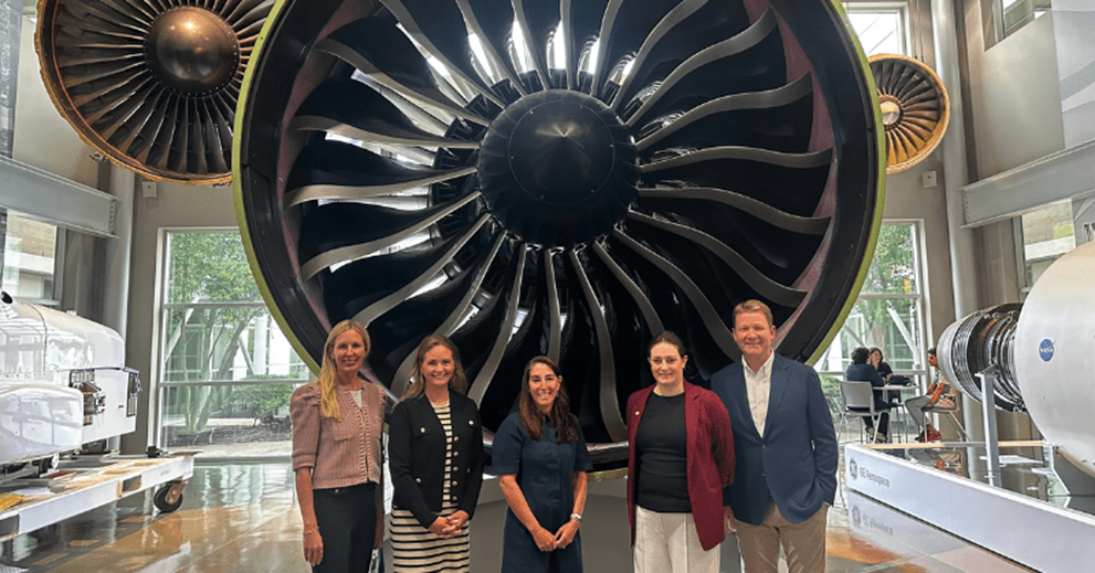 Hammack (center) poses in front of a jet engine at the GE Aerospace facility. Also pictured, from left to right, are Karin Burns (Southwest Ohio and Northern Kentucky Business Advisory Council member) and Shannon Mann, both from GE Aerospace; Julianne Dunn of the Cleveland Fed; and Pete Giambastiani of GE Aerospace.