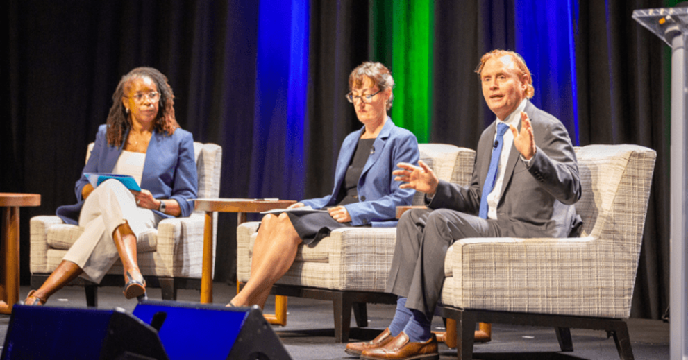 Three people seated on chairs on a stage.