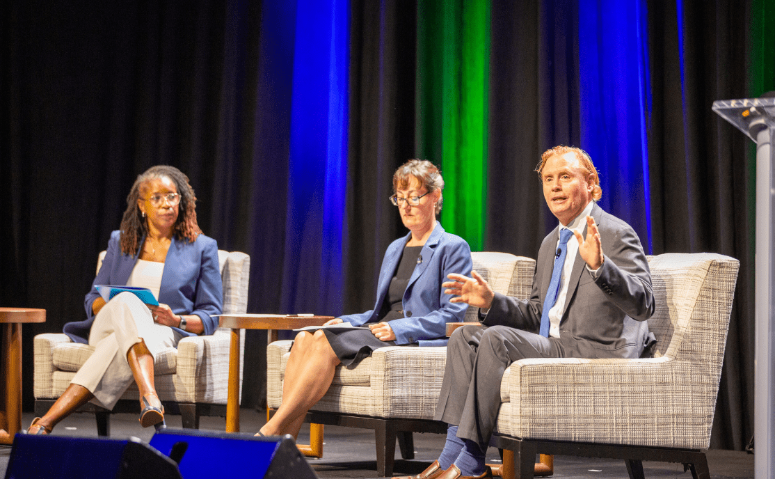Three people seated on chairs on a stage.
