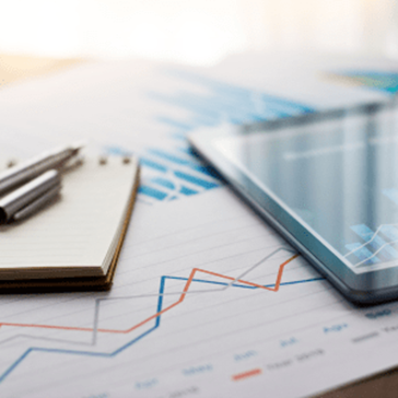 A printed graph with a notebook, pens, and a tablet sitting on top.