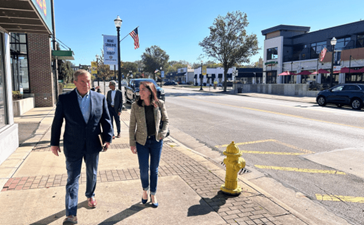 A man and a woman walk down the street in the center of a town.