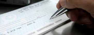 Someone holding a pen over a checkbook.