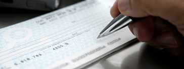 Someone holding a pen over a checkbook.